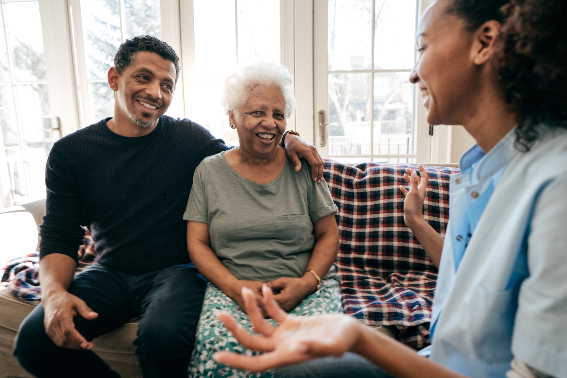 Older woman seated with two companions in a sunny living room.